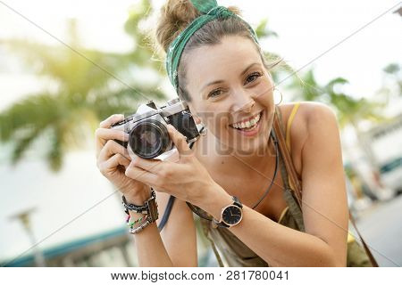 Portrait of stylish young woman taking photos with vintage camera in urban setting