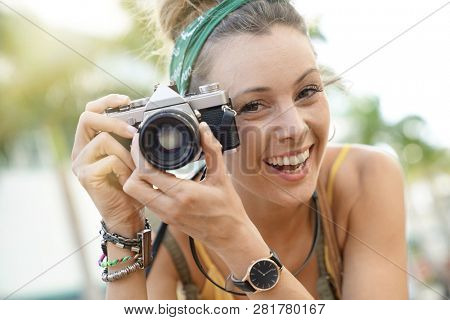 Portrait of stylish young woman taking photos with vintage camera in urban setting