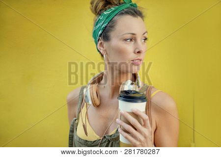 Styllish young woman with takeaway coffee outdoors on coloured background