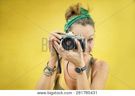 Young stylish woman taking photos outdoors with vintage camera on colored background