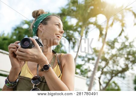 Stylish young woman taking photos with vintage camera surrounded by palm trees