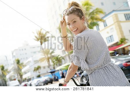 Smiling young woman on bicylce in palm tree adorned city