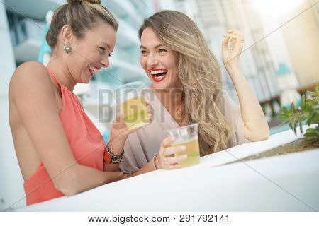 Two attractive funloving friends partying with drinks on rooftop bar in city
