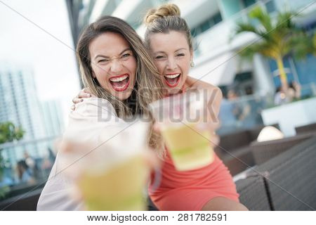 Two attractive funloving friends partying with drinks on rooftop bar in city