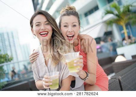 Two attractive funloving friends partying with drinks on rooftop bar in city