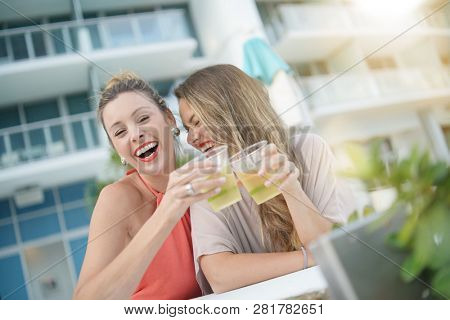Two attractive funloving friends partying with drinks on rooftop bar in city