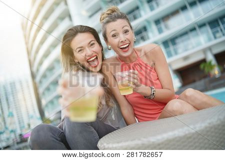 Two attractive funloving friends partying with drinks on rooftop bar in city