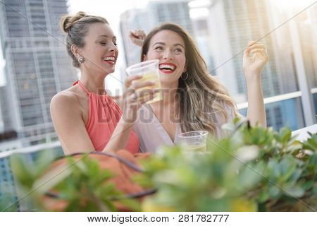 Two attractive funloving friends partying with drinks on rooftop bar in city