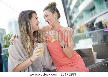 Two attractive funloving friends partying with drinks on rooftop bar in city