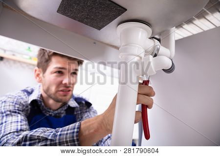 Young Male Plumber Repairing Sink Pipe With Adjustable Wrench