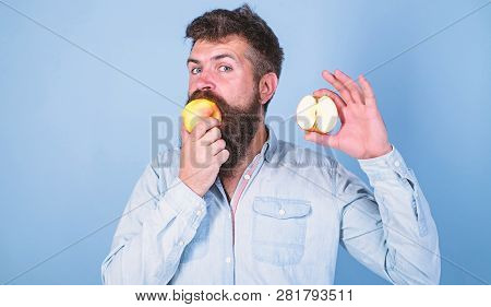 Man Bearded Eats Fruit, Holds Apple Blue Background. Half Of Apple Healthy Lifestyle. Nutritional Va