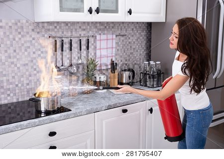 Woman Using Fire Extinguisher To Stop Fire On Burning Cooking Pot In The Kitchen