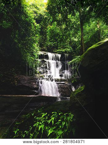Peaceful Wide Waterfall Cascade In Dense Shady Tropical Forest With Hard Rock And Blur Mossy Boulder