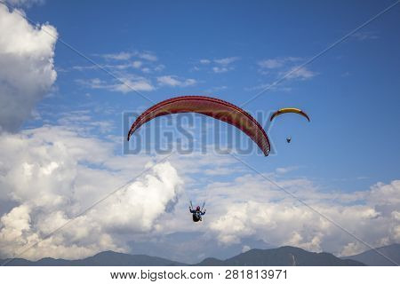 Aerial View Of Two Pargliders On Red Yellow Parachutes Flying In A Blue Sky With White Clouds Over T