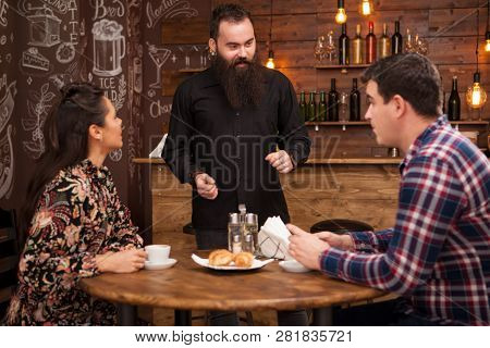 Cheerful Bearded Young Barman Laughing And Talking To Clients In Restaurant.