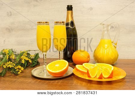 Two Glasses Of Mimosa Cocktail, A Bottle Of Champagne, A Decanter With Orange Juice, Fresh Oranges A
