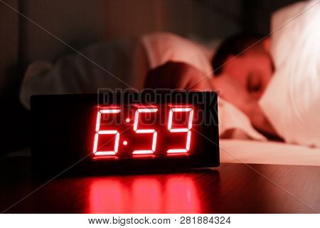 Rectangular Alarm Clock On The Bedside Table With Red Numbers, Sleeping Man In Bed In Dark Room. Con
