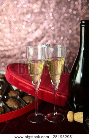 Valentines Day Champagne and Chocolates. Heart shaped velvet covered box of chocolates with roses and champagne with plastic champagne glasses. Room for text. 
