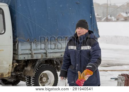 Portrait Of An Assembler Worker In A Jacket With A Hood And A Black Knitted Hat On His Head Against 