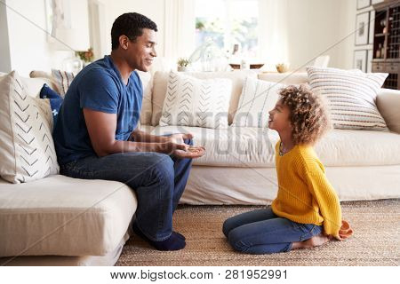 Pre-teen girl kneeling in front of her dad to give him a present she has made, close up, side view