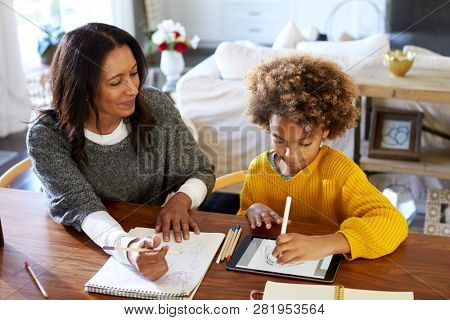 Middle aged mixed race woman sitting at a table in the dining room drawing with her granddaughter, who is using a tablet computer, elevated view, close up