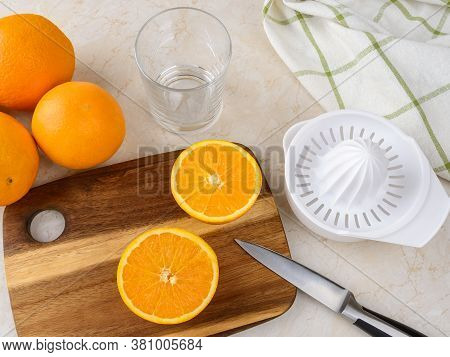 Ripe Orange Cut In Half, Plastic Manual Citrus Juicer, Fruit Knife And Empty Glass On The Kitchen Ta