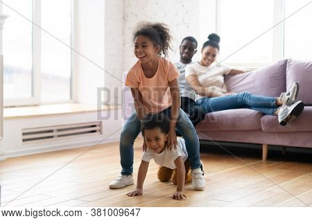 Happy Married Couple Watching Their Children Playing Leapfrog On Floor