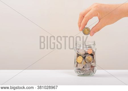White Hand Man Holding Gold Coin To Putting In Jar Or Glass Bottle For Saving With Soft White Backgr
