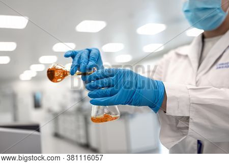 Flasks With Brown Liquid In Scientist Hands With Dropping Chemical Liquid To Test Tubes, Science And
