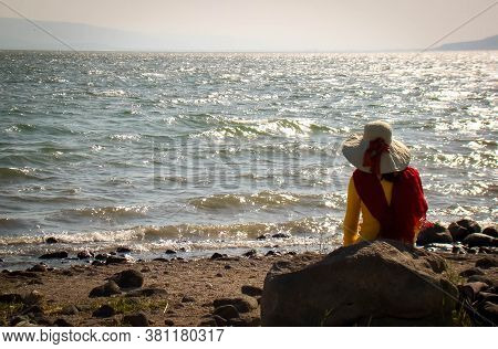 Amazing Woman Using A Hat Contemplating Sea Of Galilea, In Israel. Loneliness And Pray