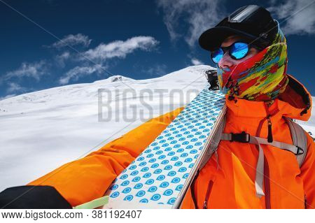 Portrait Of A Stern Climber Skier In Sunglasses And A Cap With A Ski Mask On His Face. Holds His Ski
