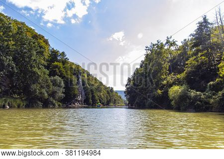 Russia City Resort. People Sail In A Rowboat Along The River Against The Mountain Rock Cockerel On A