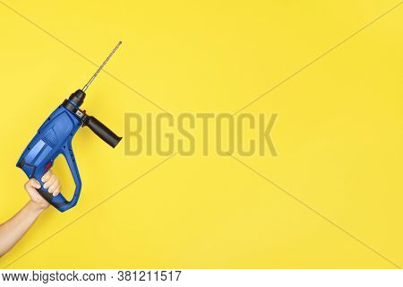 Blue Puncher In The Hands Of A Builder. Female Hand Hold New Puncher Or Drill Isolated On Yellow Bac