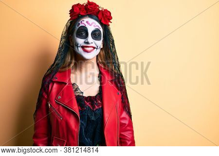 Woman wearing day of the dead costume over yellow looking positive and happy standing and smiling with a confident smile showing teeth 