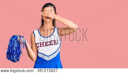 Young beautiful woman wearing cheerleader uniform smiling and laughing with hand on face covering eyes for surprise. blind concept. 