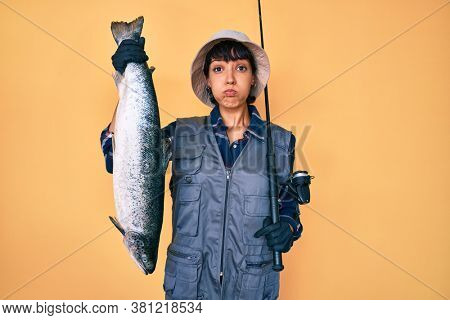 Beautiful brunettte fisher woman holding fishing rod and raw salmon puffing cheeks with funny face. mouth inflated with air, catching air. 