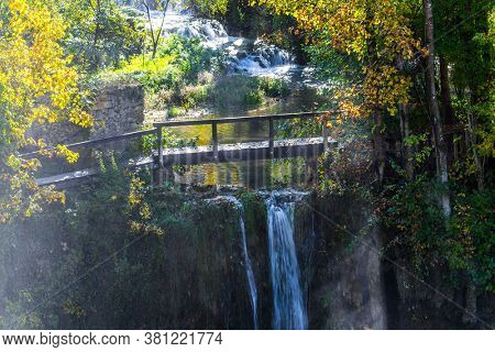 Sun rays over a wooden small bridge and a waterfall. The Croatian town of Slunj. Cascade of waterfalls on the Sluncica River. The concept of ecological, active and photo tourism