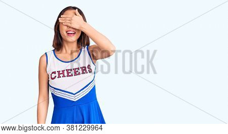 Young beautiful chinese girl wearing cheerleader uniform smiling and laughing with hand on face covering eyes for surprise. blind concept. 