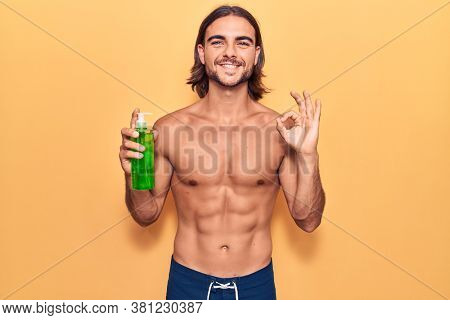 Young handsome man wearing swimwear holding aloe vera doing ok sign with fingers, smiling friendly gesturing excellent symbol 