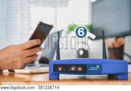 Closeup Of A Wireless Router With Wifi 6 Technology And A Man Using Smartphone On Living Room At Hom