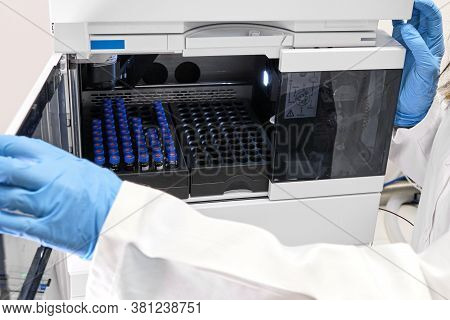 Scientist In A White Lab Coat Putting Vial With A Sample Into Autosampler Of Hplc System. High Perfo