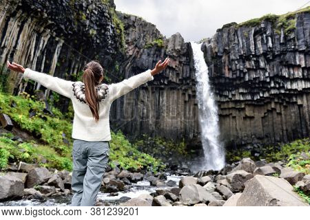 Iceland. Woman enjoying majestic Svartifoss waterfall. Female is visiting famous tourist attraction of Iceland. Spectacular natural landmark on vacation in Skaftafell. Icelandic nature landscape.
