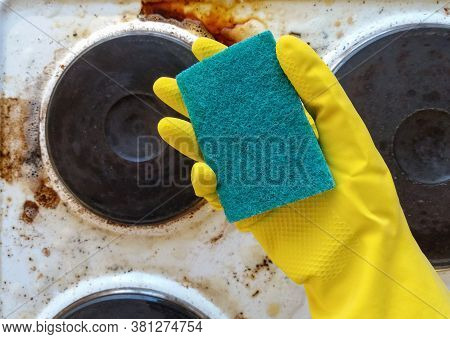Hand In Yellow Glove Holding Washup Sponge Against Dirty Electric Stove