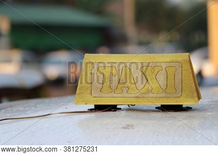 Taxi Light Sign Or Cab Sign In Drab Yellow Color With Peel Text On The Car Roof At The Street Blurre