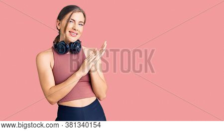 Beautiful caucasian young woman wearing gym clothes and using headphones clapping and applauding happy and joyful, smiling proud hands together 