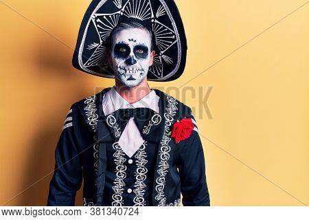 Young man wearing mexican day of the dead costume over yellow looking positive and happy standing and smiling with a confident smile showing teeth 