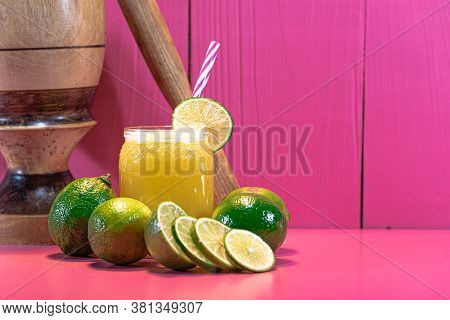 Lemon Juice And Lemonade (citrus Aurantifolia) Amid Wooden Pestle And Fresh Fruits On Pink Backgroun