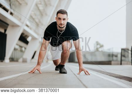 Young Strong Brunette Man In Sportswear On Ready Position To Run On The Street Stadium Listens His F