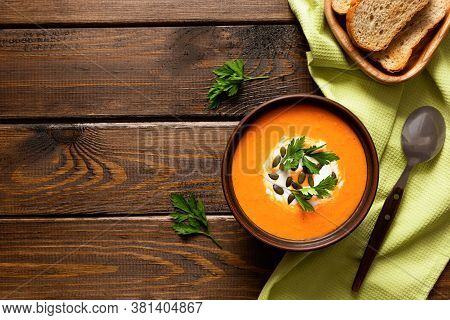 Pumpkin Cream Soup, Served With Crackers And Parsley On A Wooden Table. Vegetarian And Vegan Food. H