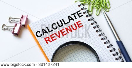 Notepad With Text Calculate Revenue On White Background With Clips, Pen And Magnifying Glass